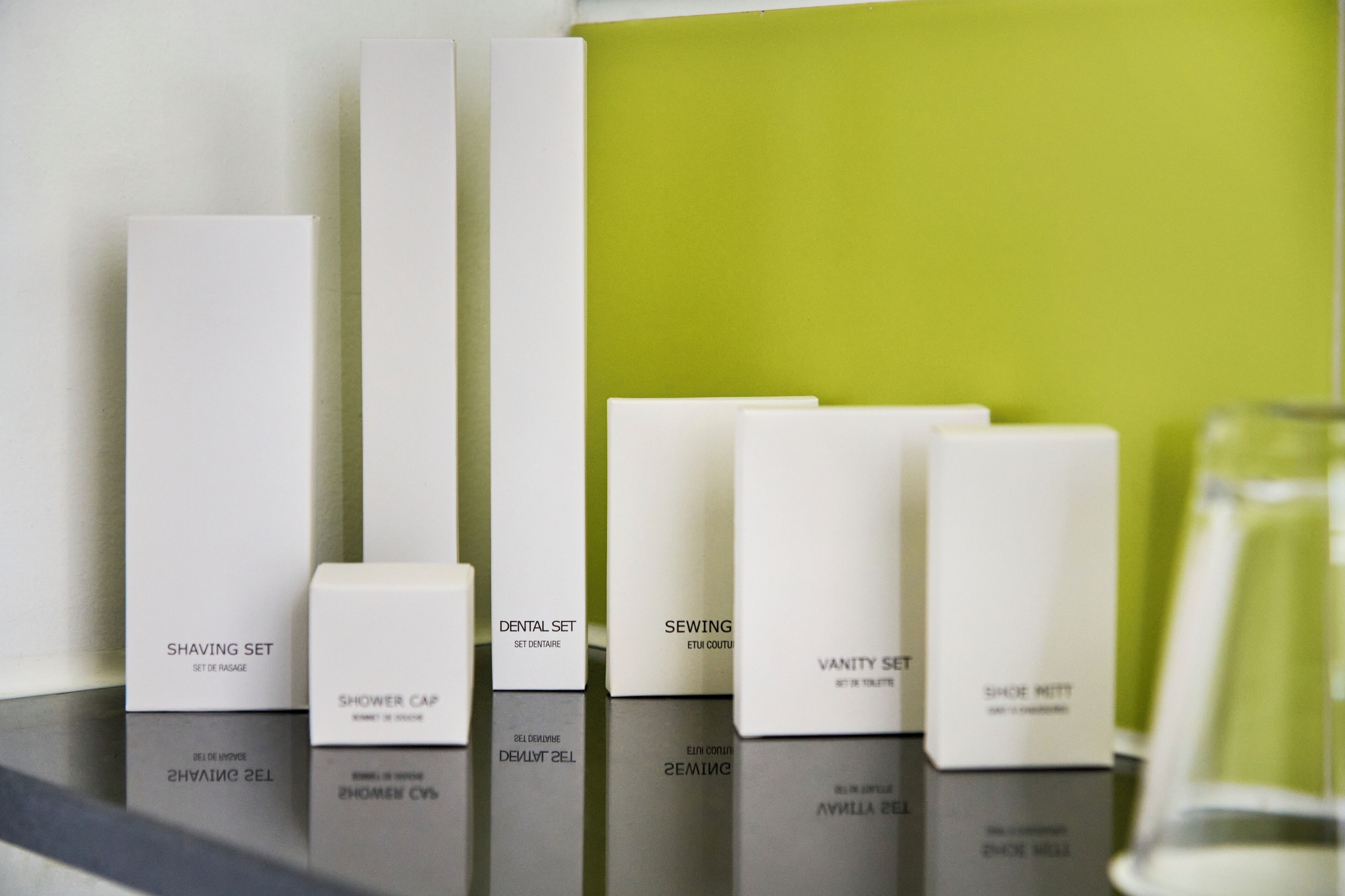 A row of white toiletry boxes on a shelf against a green wall.