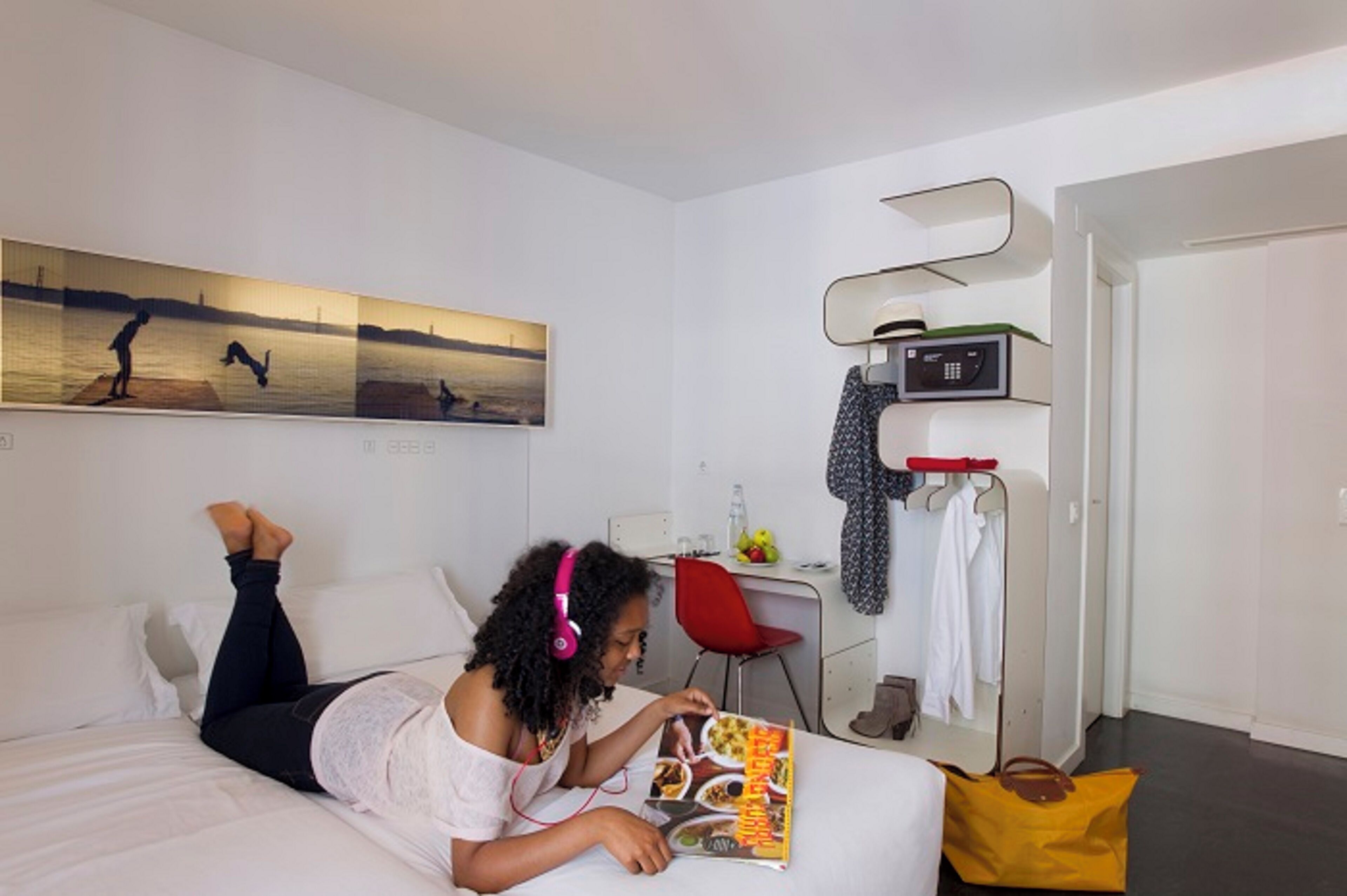 Una habitación de hotel con cama, escritorio, silla, perchero y microondas.