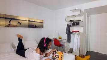 Una habitación de hotel con cama, escritorio, silla, perchero y microondas.