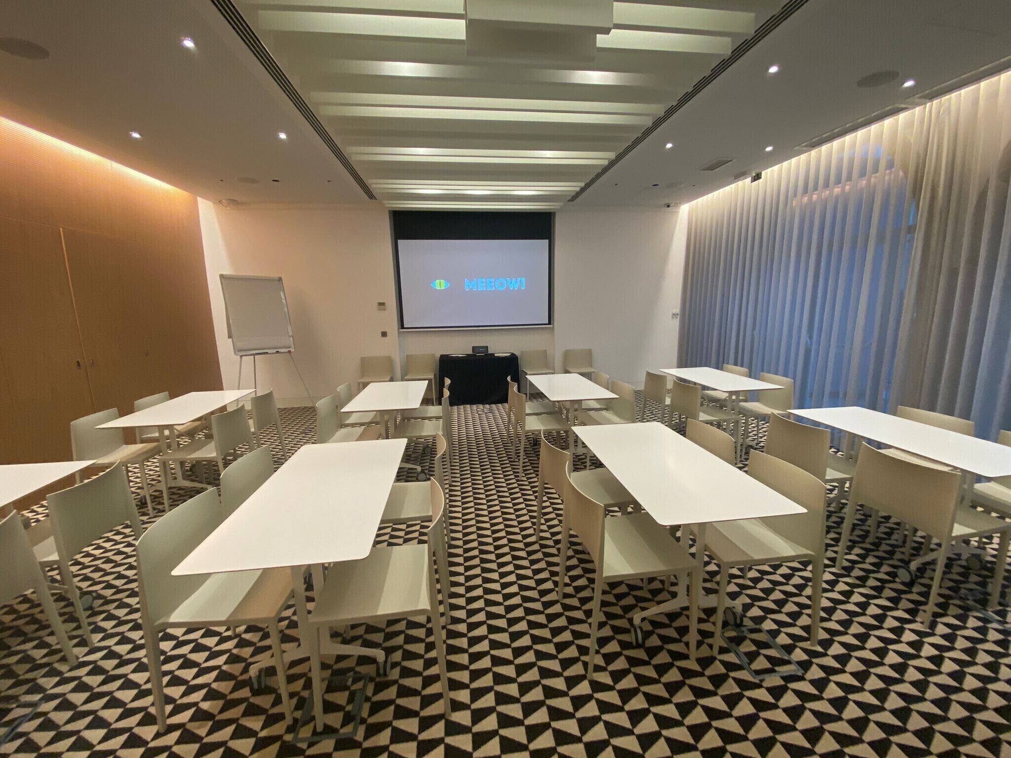 A conference room with white tables and chairs, a projector screen displaying 'MEOW!', and a patterned floor.