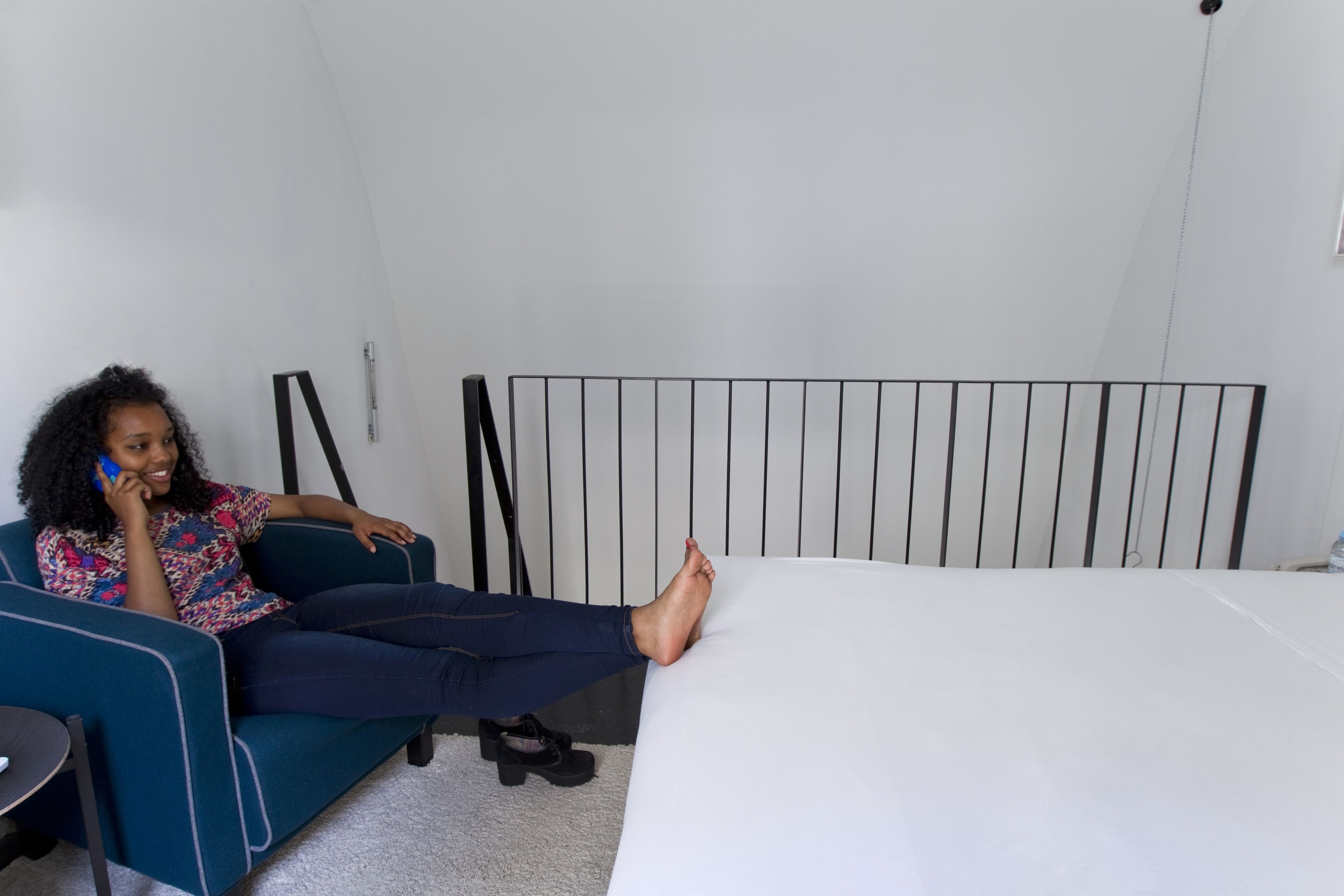 A person sitting on a blue couch in a room with a white bed and a black headboard.