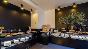 Montaje tipo bufé con diversos alimentos y platos, una planta grande en maceta y una cocina moderna.