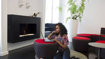 A modern lounge area with a fireplace, red ottomans, and a laptop on a red stool.