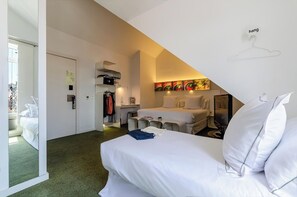 Ett hotellrum med en säng, ett skrivbord, en stol, en klädställning och en tavla på väggen.