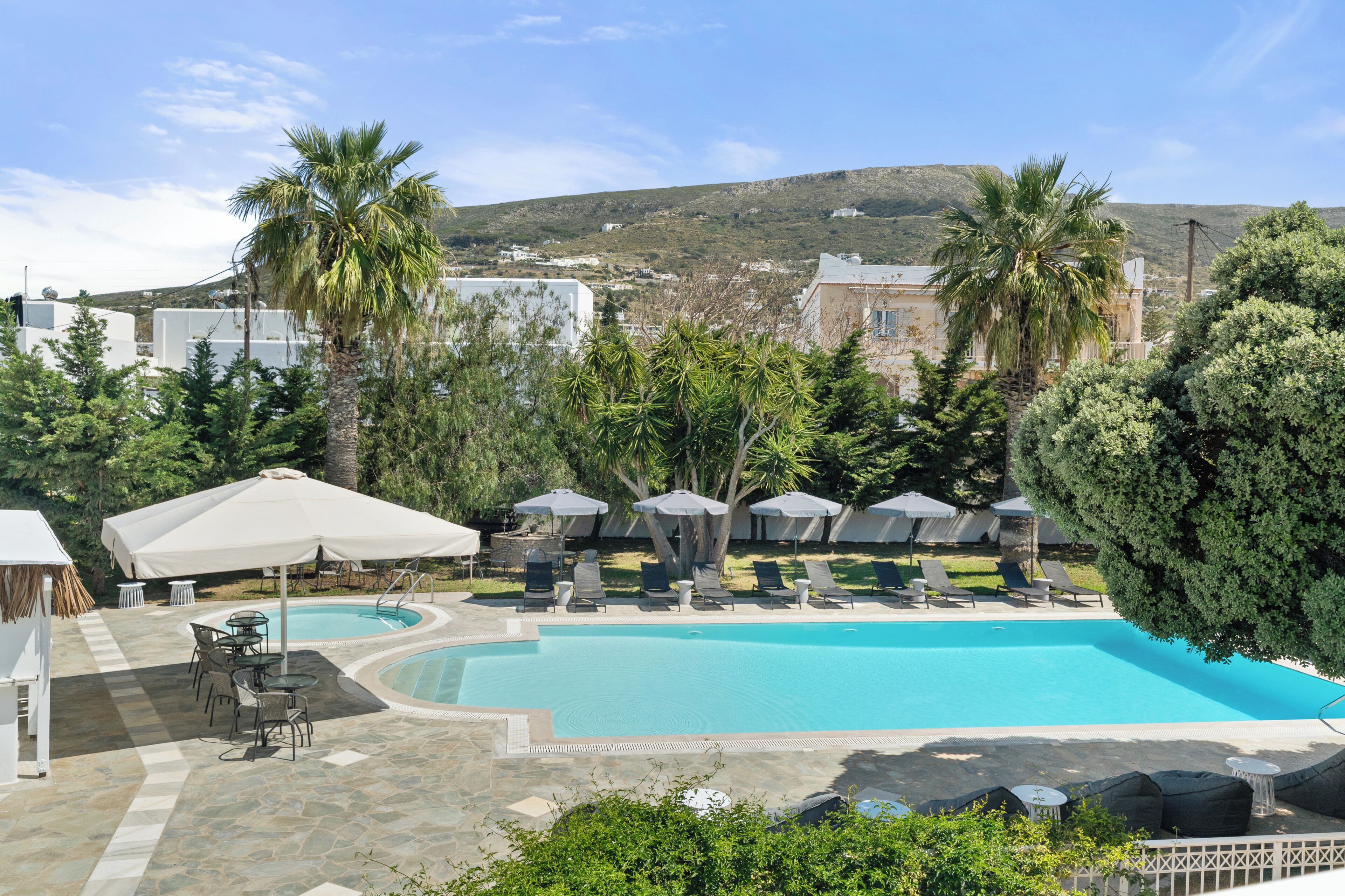 A swimming pool with lounge chairs and umbrellas, surrounded by greenery and buildings in the background.