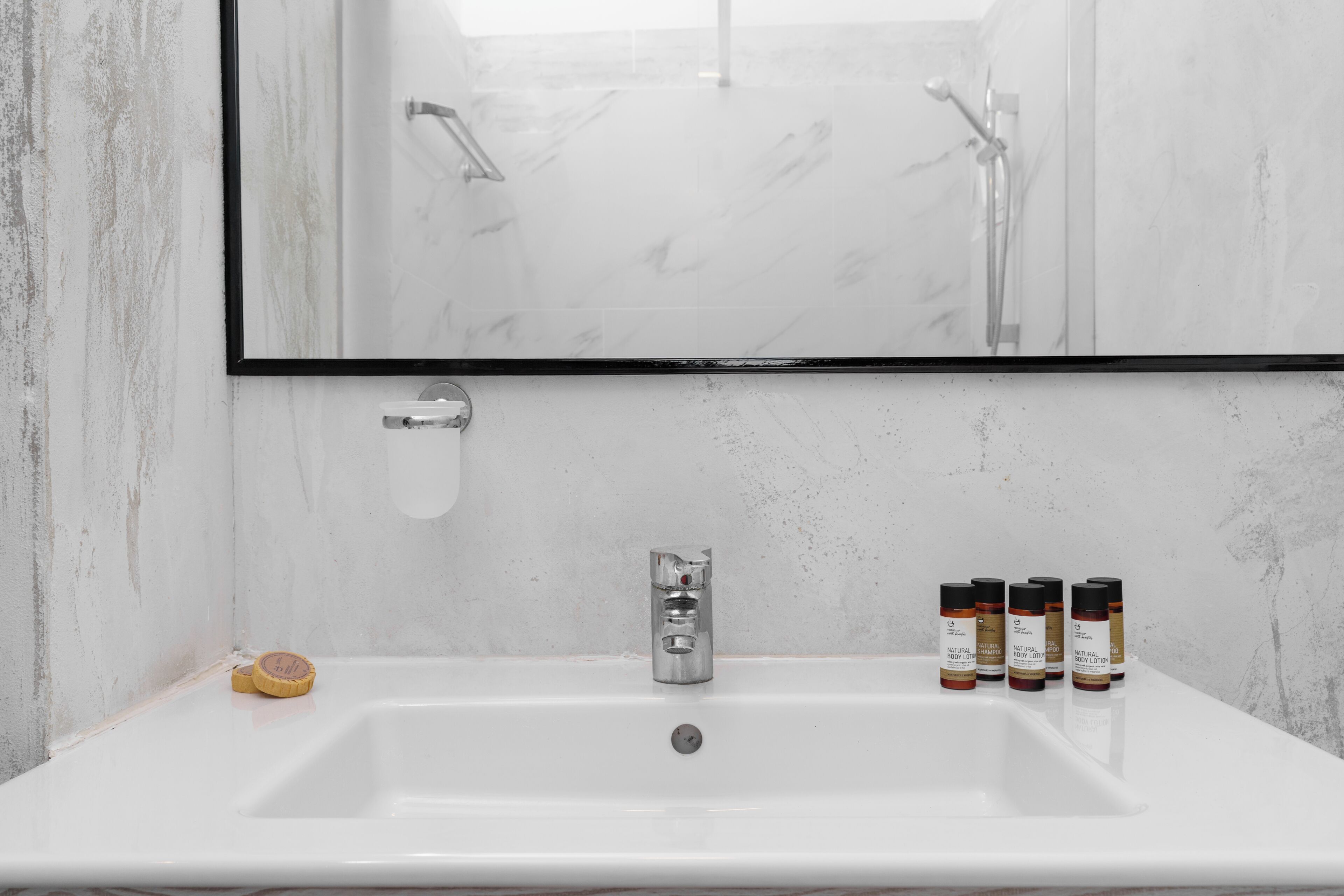A bathroom with a white sink, a mirror, and four bottles of lotion.