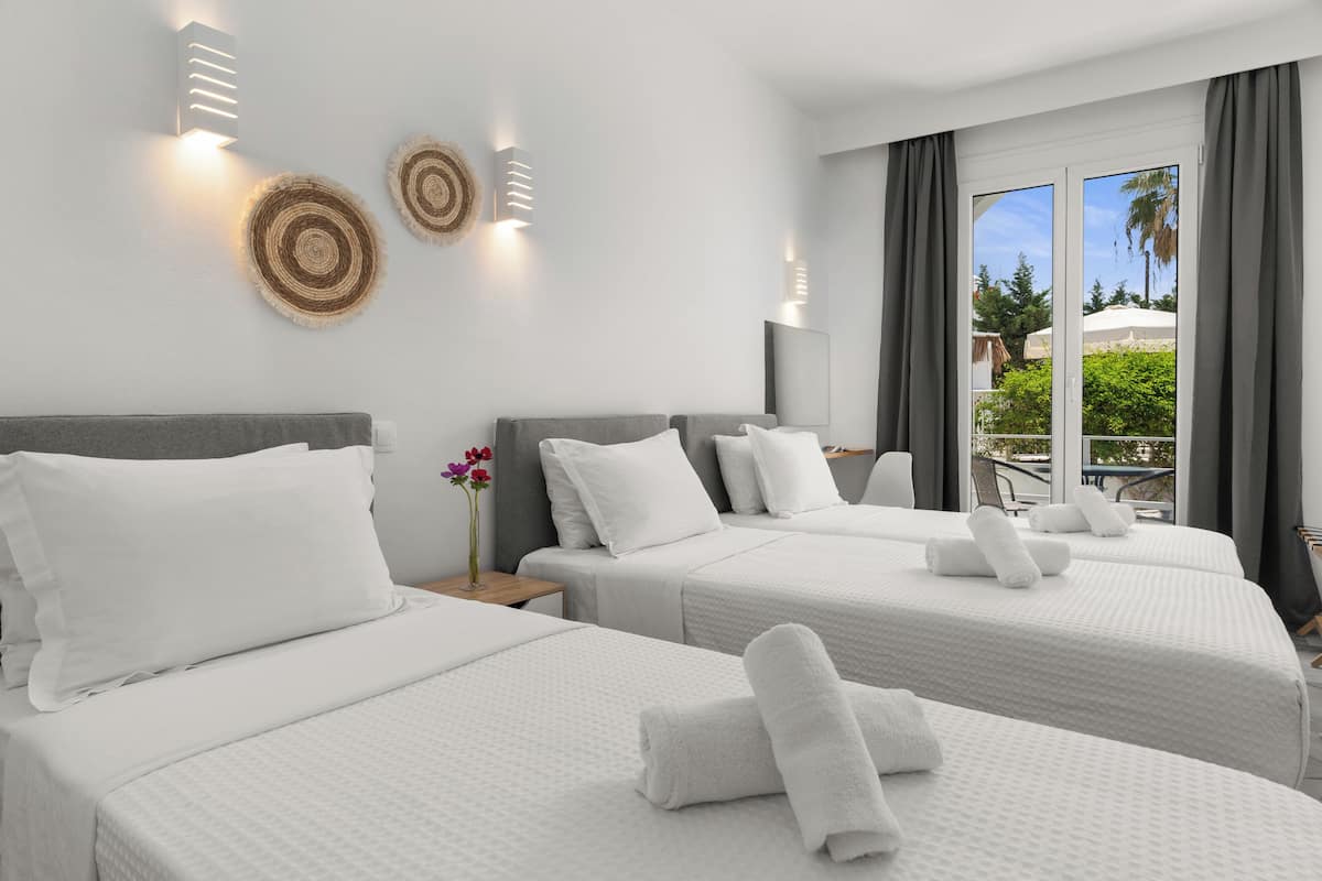 A hotel room with three beds, a large window with a view, and a wall-mounted light fixture.