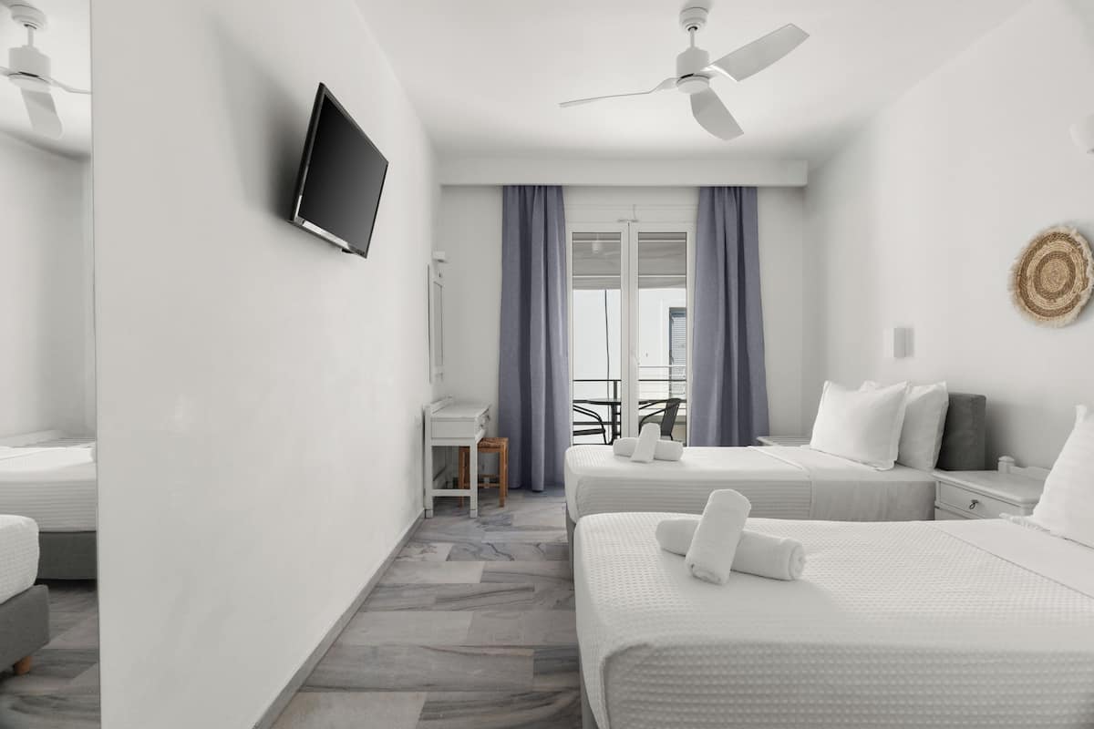 A hotel room with two beds, a desk, a chair, a TV, and a ceiling fan.