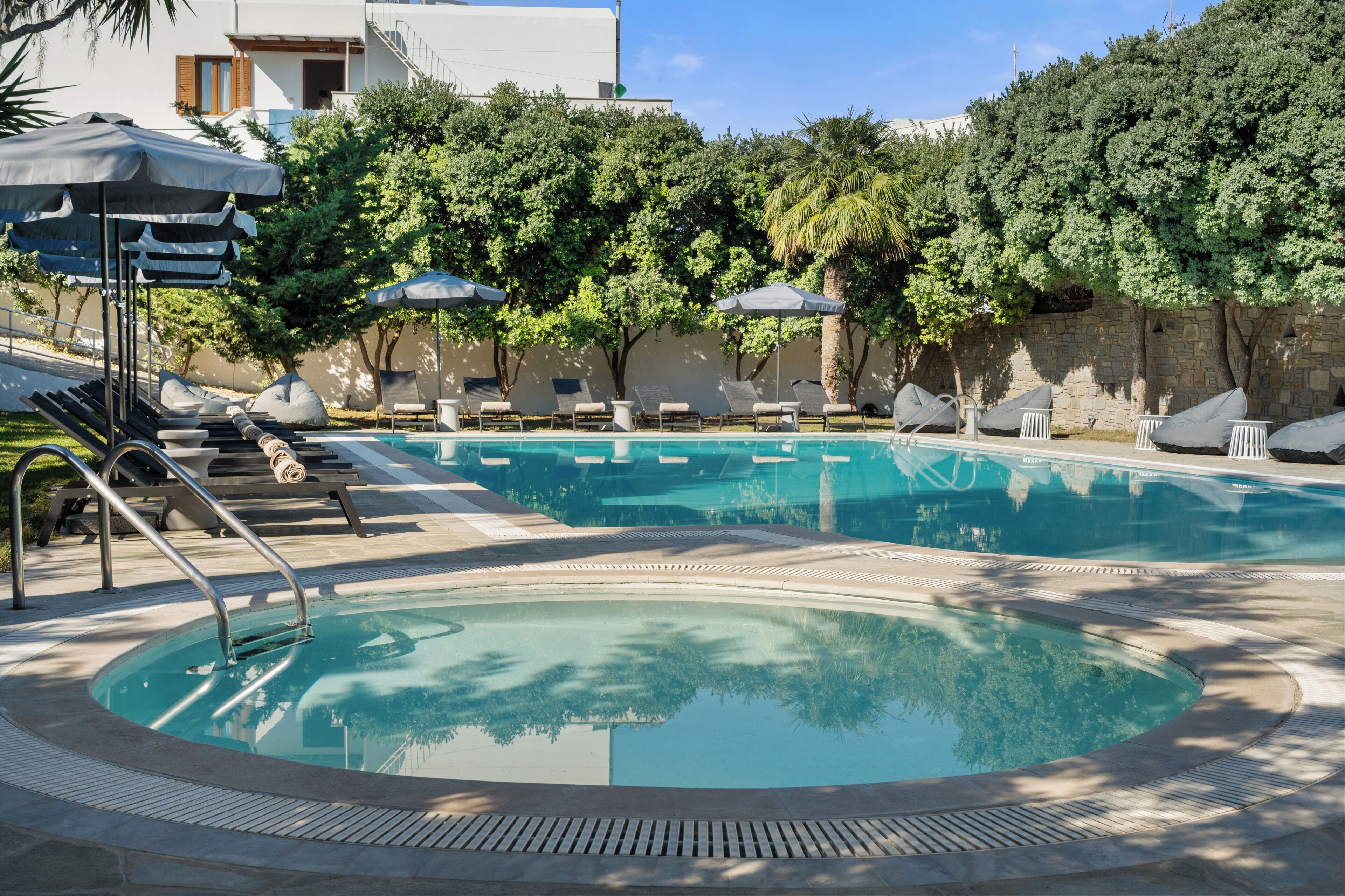 A swimming pool with lounge chairs and umbrellas, surrounded by trees and a building.