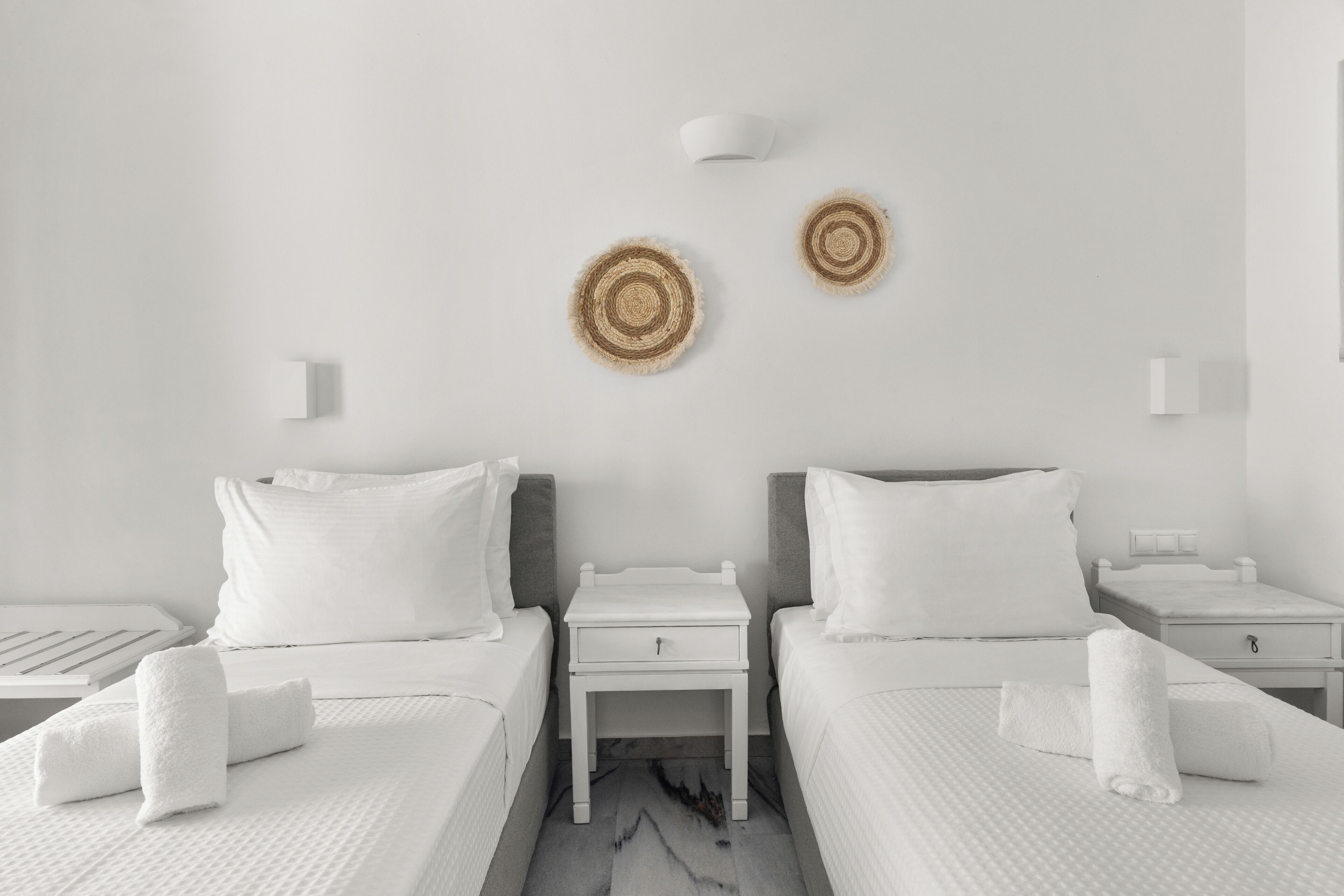 A hotel room with two beds, white bedding, a small bedside table with a lamp, and a wall-mounted light fixture.