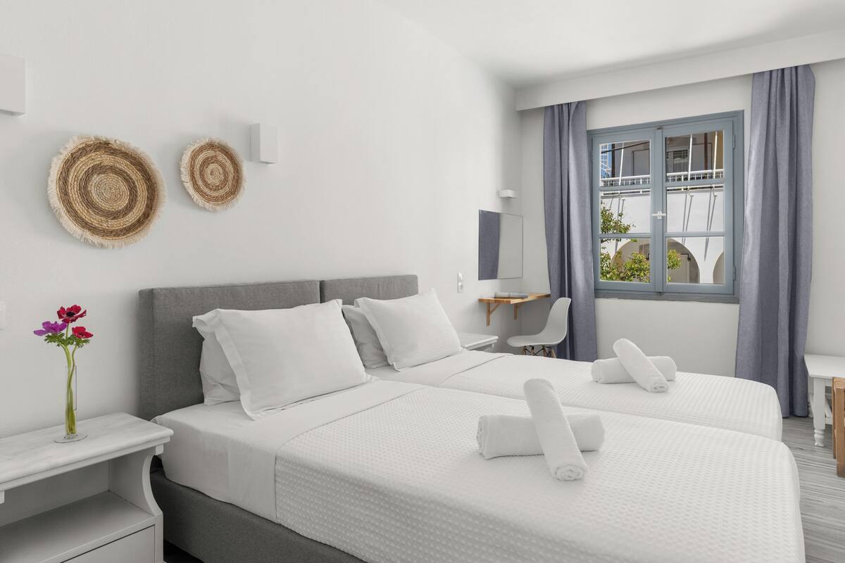 A hotel room with two beds, a desk, a chair, a window with curtains, and wall decor.