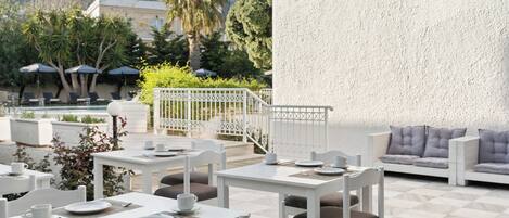An outdoor dining area with white tables and chairs, a white sofa, and a white wall.