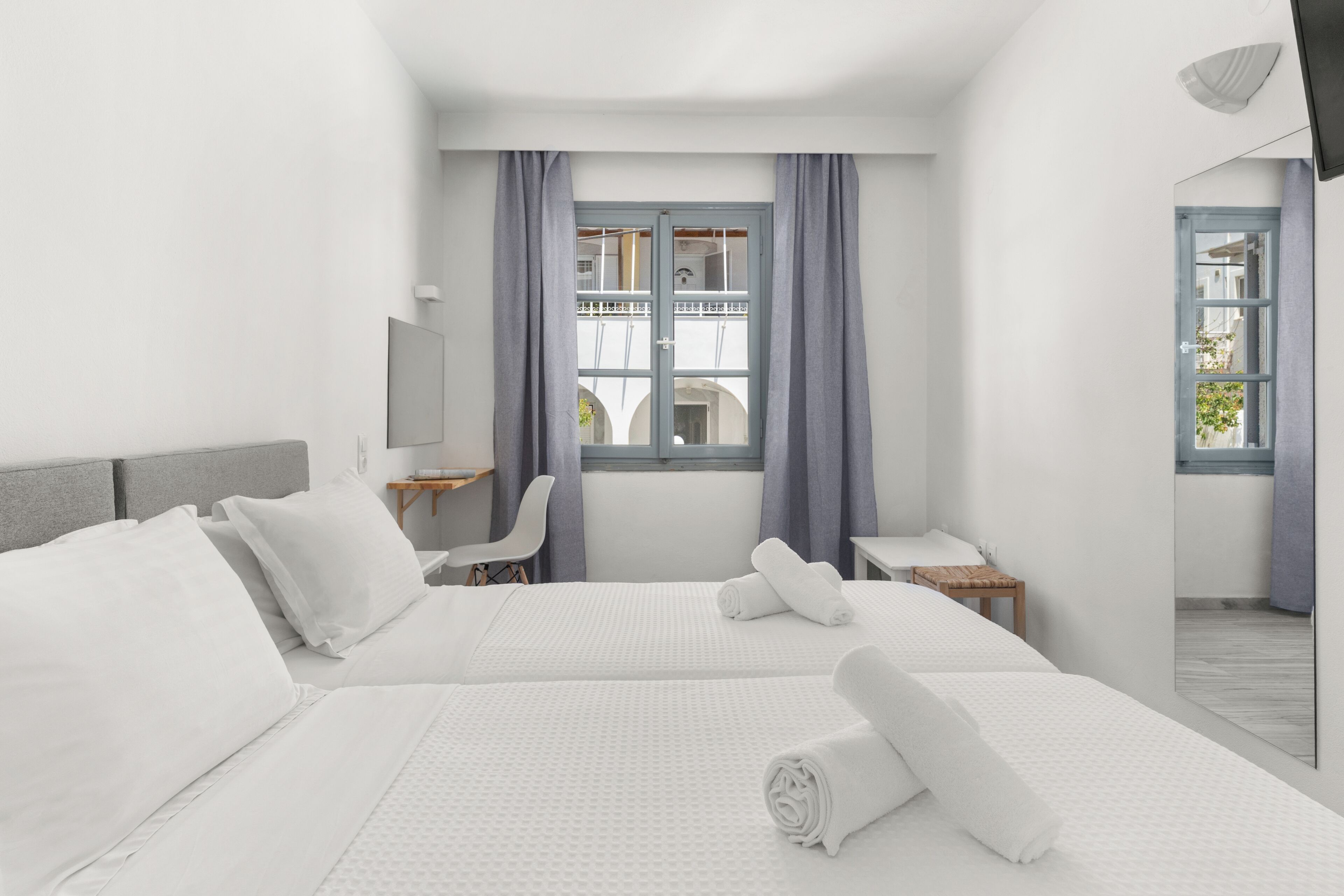 Quarto de hotel com duas camas, uma escrivaninha, uma cadeira, uma televisão e uma janela com cortinas.