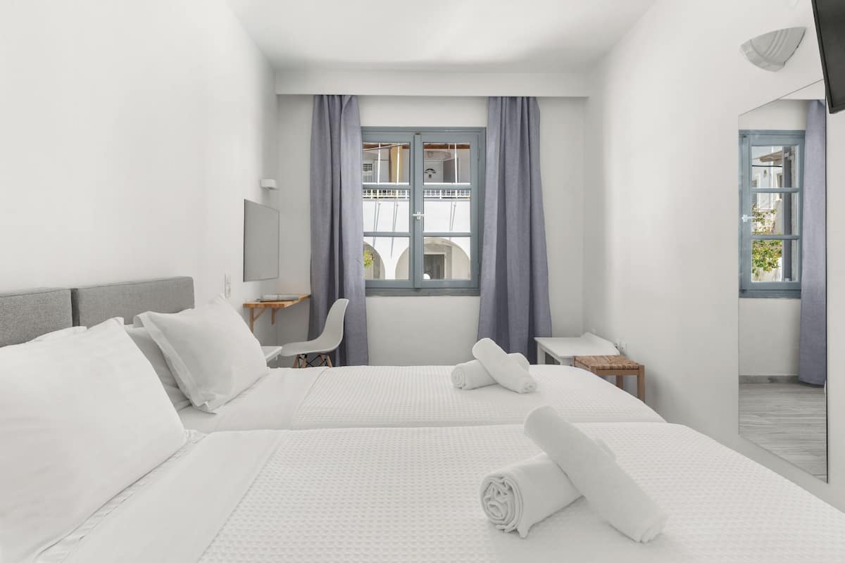 Quarto de hotel com duas camas, uma escrivaninha, uma cadeira, uma televisão e uma janela com cortinas.