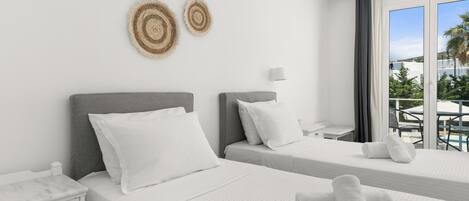 Habitación de hotel con dos camas, una mesita de noche, una lámpara y vistas al exterior.