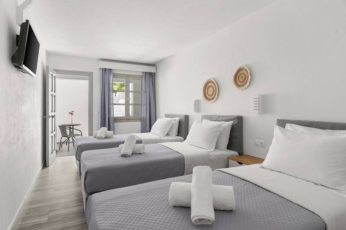 A hotel room with three beds, a TV, a small table, and a window with curtains.
