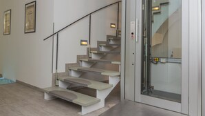 A modern staircase with a glass door at the top, leading to a room with a light-colored floor and a white wall. - Dan In'n Out (Vienna)