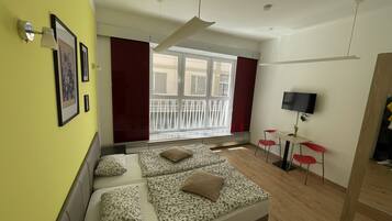 Une chambre moderne avec un grand lit, une télévision et une fenêtre donnant sur des immeubles.