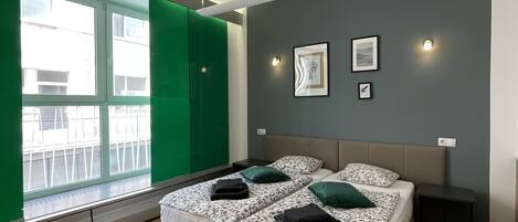 Een moderne slaapkamer met een groot bed, twee nachtkastjes, een raam met groene gordijnen en een wandlamp.