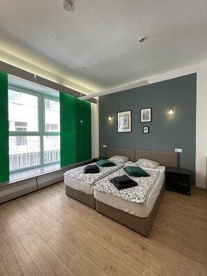A modern bedroom with a large bed, two bedside tables, a window with green curtains, and a wall-mounted light fixture.
