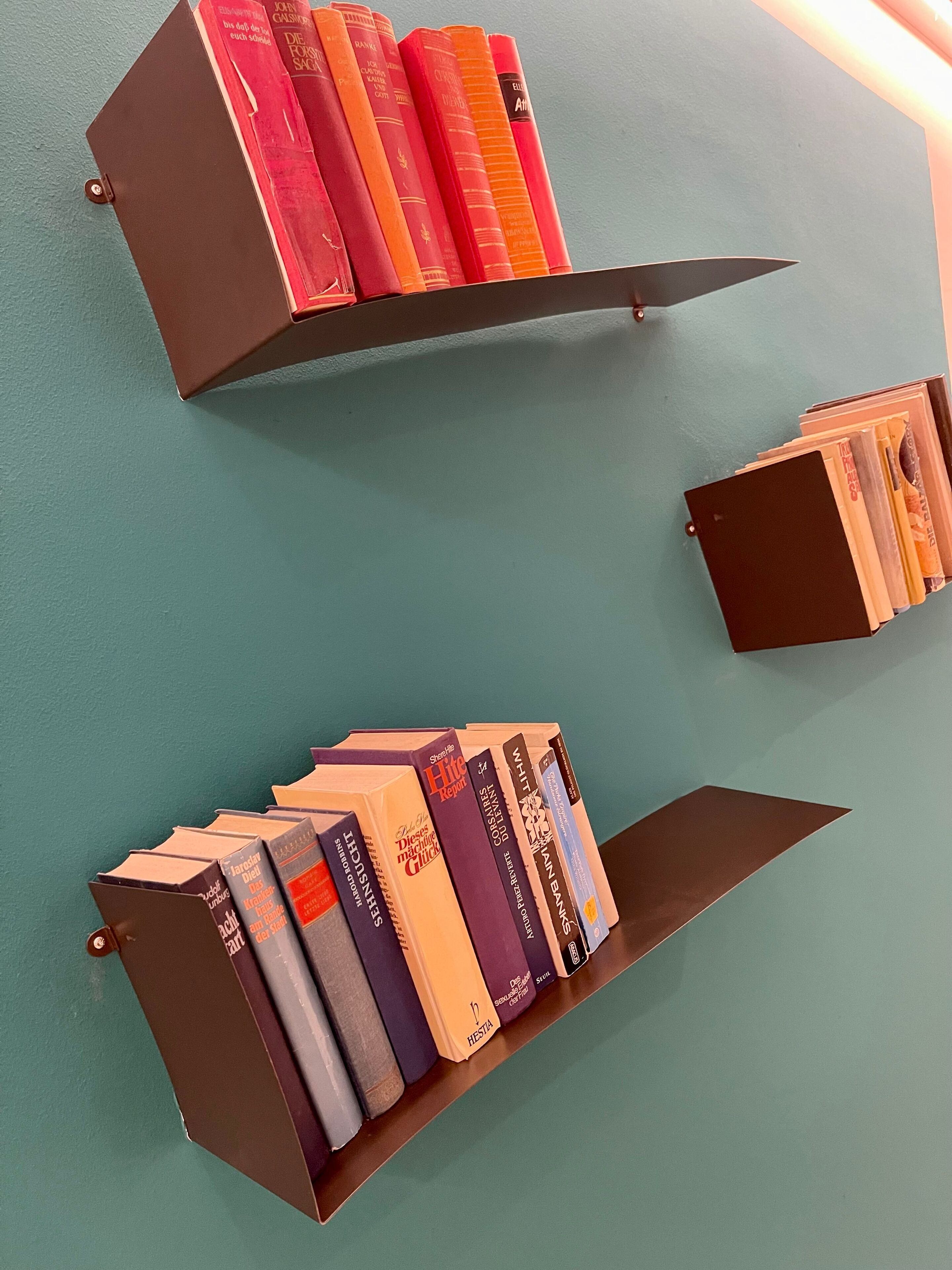 Two bookcases with books against a teal wall.