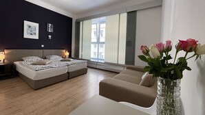 A modern bedroom with a bed, a sofa, a vase with flowers, and a window with blinds. - Dan In'n Out (Vienna)