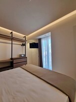 A hotel room with a bunk bed, a flat-screen TV mounted on the wall, and a window with curtains.
