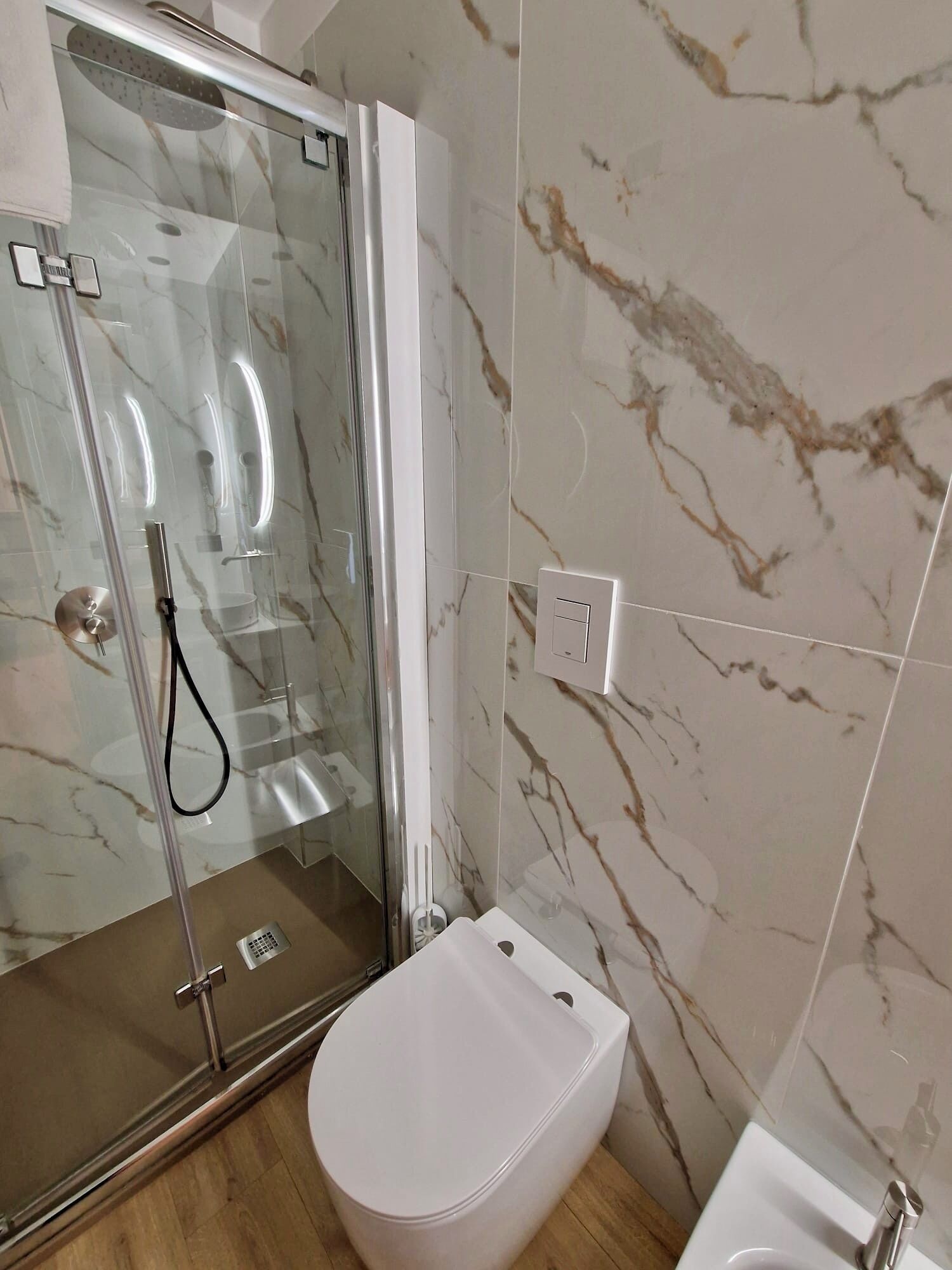 A bathroom with a glass-enclosed shower, a white toilet, and marble-patterned walls.