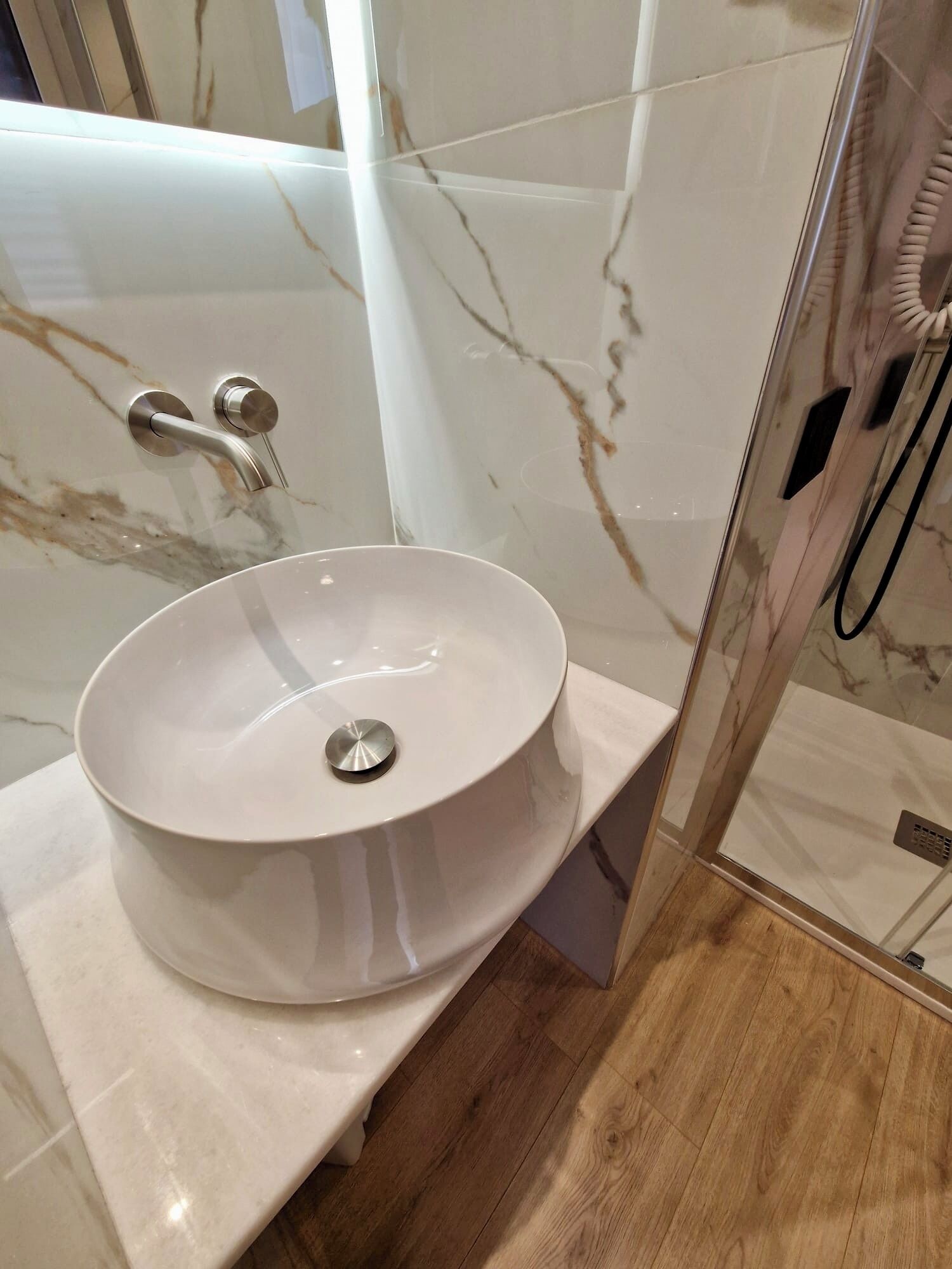 Ein Badezimmer mit einem weißen Marmorwaschbecken, einer Duschkabine und Holzboden.