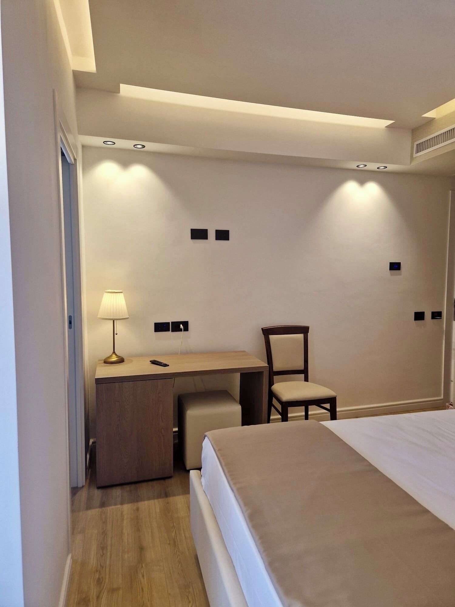 Habitación de hotel con cama, escritorio, silla, lámpara y una pequeña mesa.