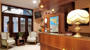 Una zona de recepción con un escritorio de madera, dos sillas ornamentadas, un mapa y un televisor en la pared.