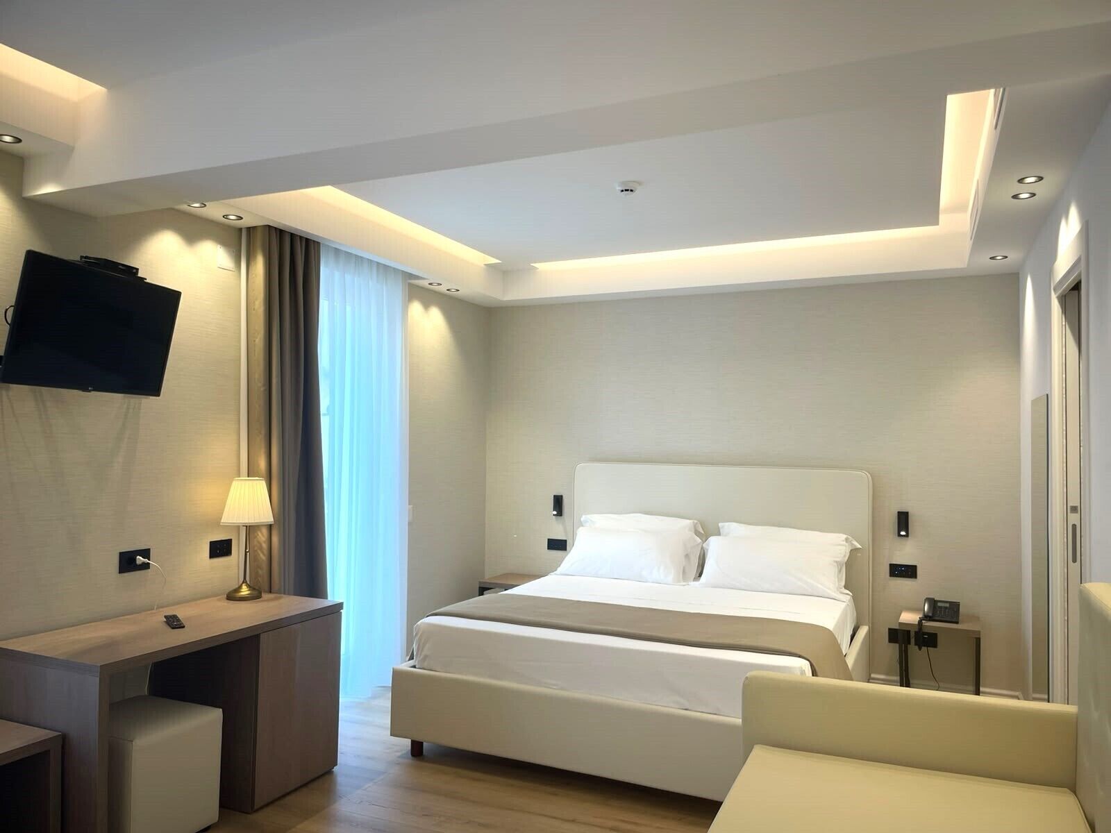 Een moderne hotelkamer met een bed, een bureau, een stoel en een aan de muur bevestigde televisie.