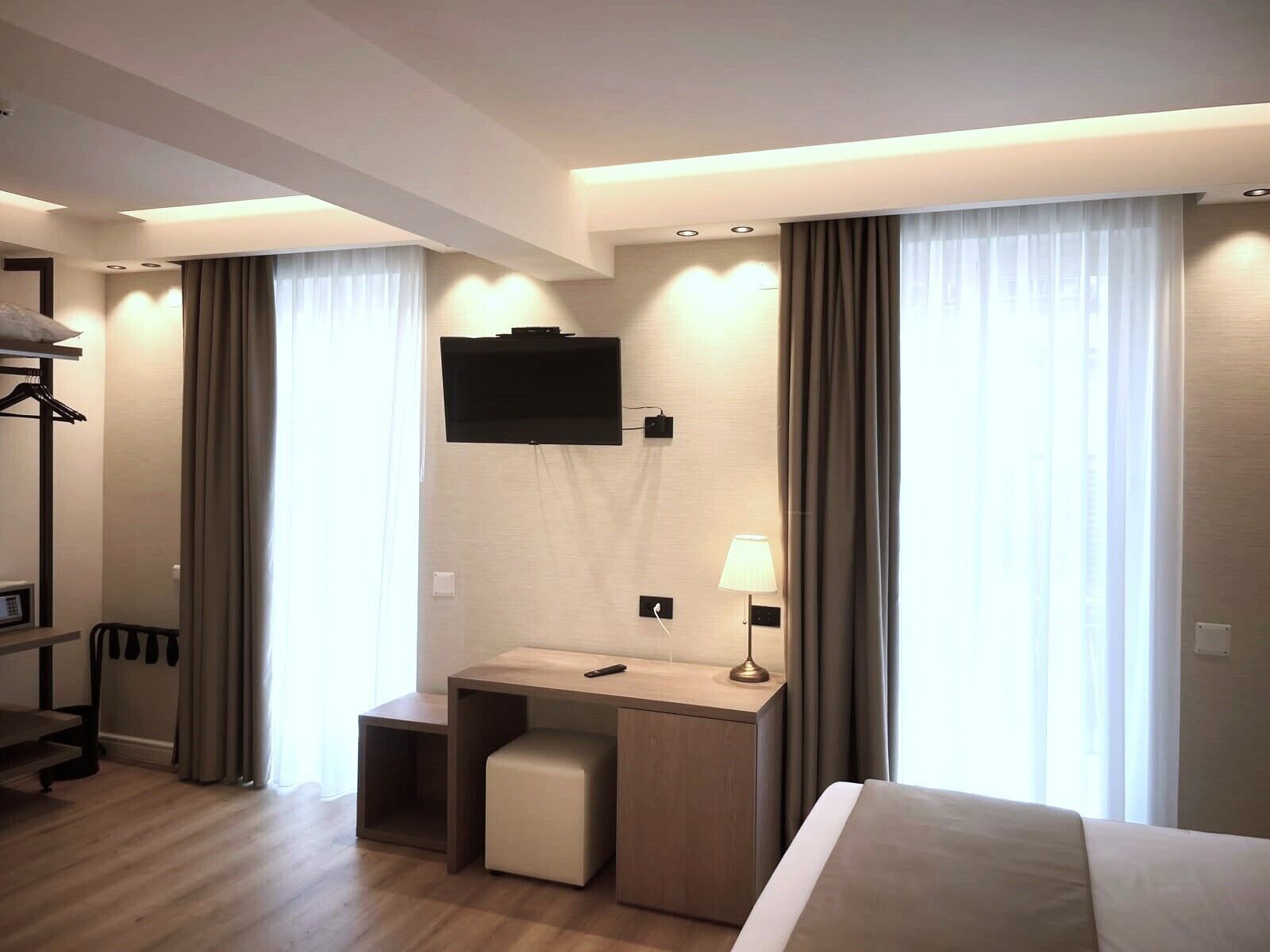 Une chambre d’hôtel comprenant un lit, un bureau avec une chaise, un téléviseur fixé au mur et une fenêtre avec des rideaux.