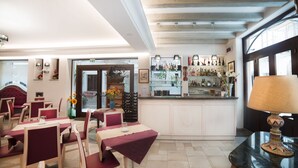 Un interior de restaurante con mesas y sillas, una zona de bar con estantes llenos de botellas, y un amplio ventanal.