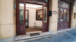 Entrada de hotel con fachada de madera, puerta de vidrio y el interior visible desde el umbral.