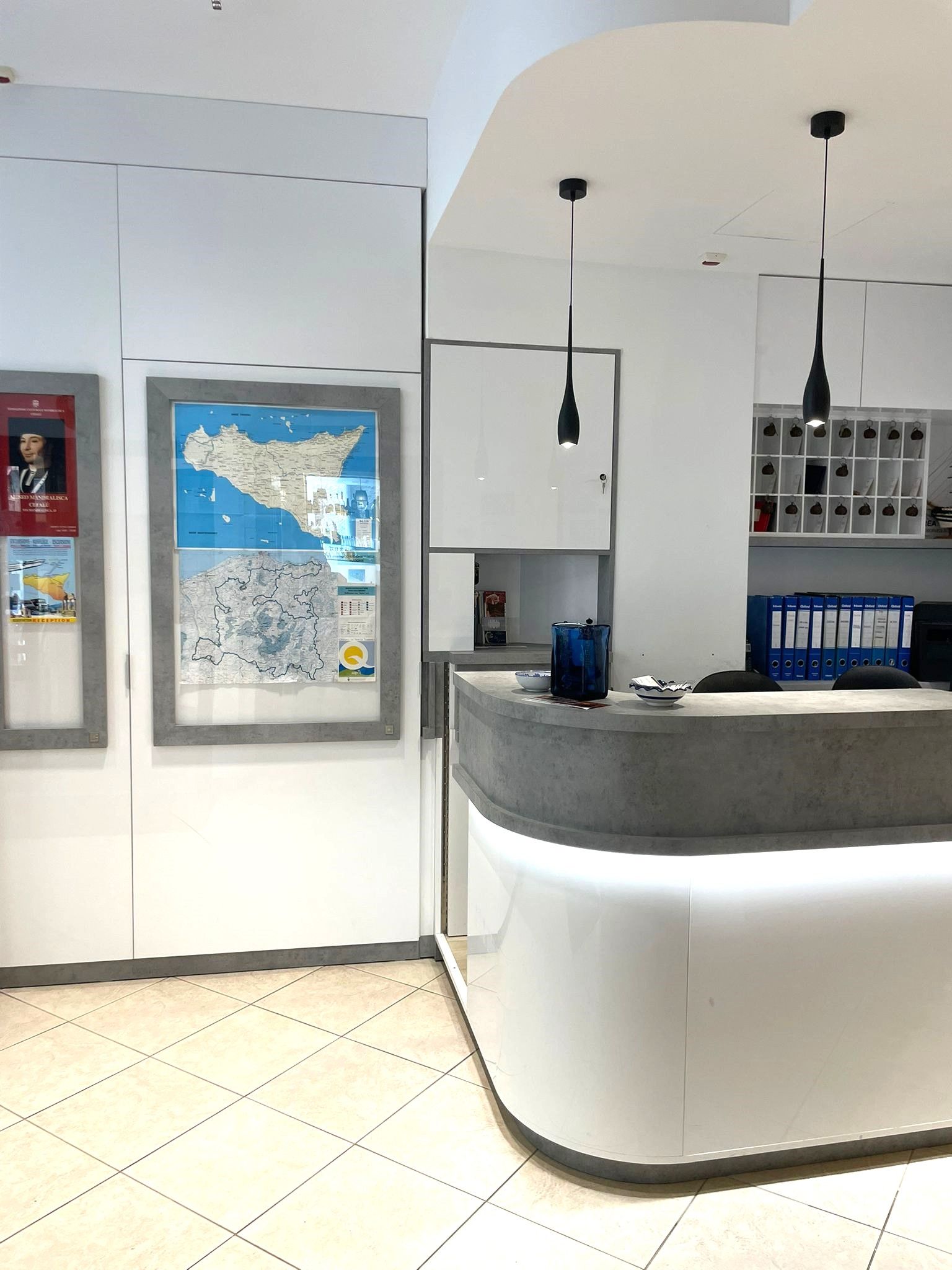 Un área de recepción con mostrador curvo, mapas enmarcados y una lámpara colgante moderna.
