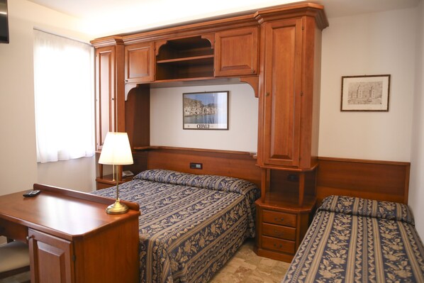 A bedroom with a wooden headboard, two beds with patterned bedding, a desk with a lamp, and a framed picture on the wall. - Hotel La Giara (Cefalù)