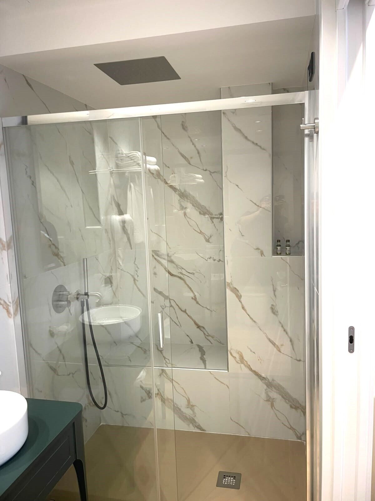 Ein modernes Badezimmer mit einer in Glas gefassten Dusche, Marmorwänden und einem Waschbecken.