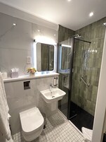 Un baño moderno con ducha de vidrio, lavamanos blanco y retrete.