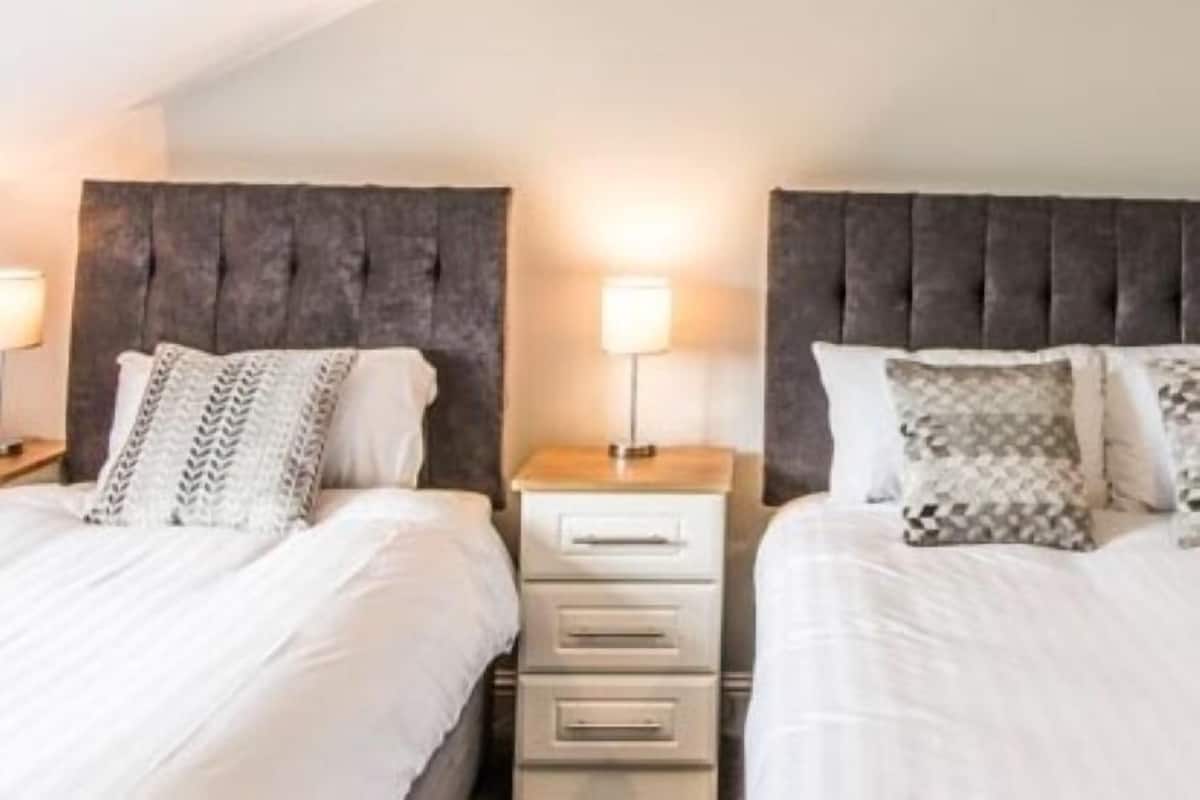 A double bed with a headboard, a bedside table with a lamp, and a drawer unit.