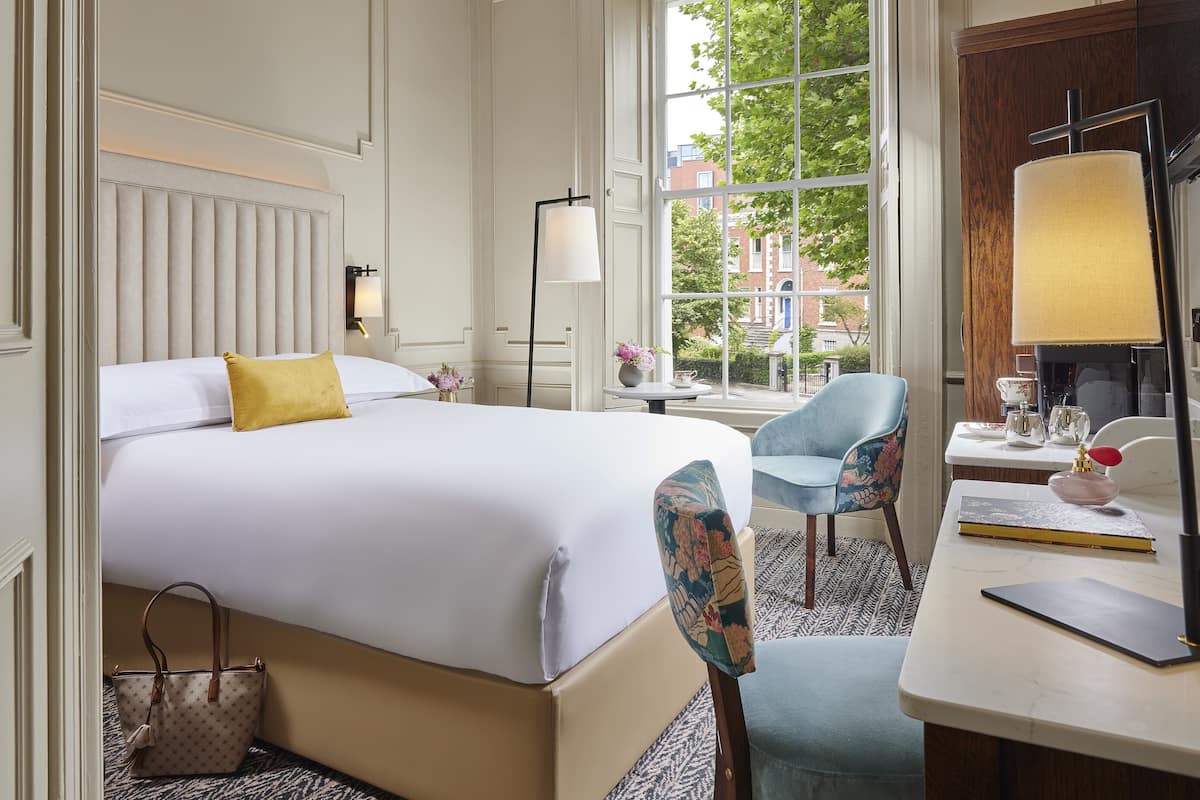 A hotel room with a large bed, a desk with a lamp, a chair, and a view of the outside.