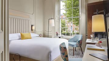 Een hotelkamer met een bed, een bureau, een stoel, een lamp en uitzicht op gebouwen door een raam.