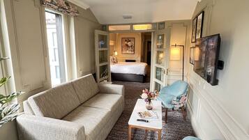 A hotel room with a sofa, a small table, two chairs, a bed, and a television mounted on the wall.