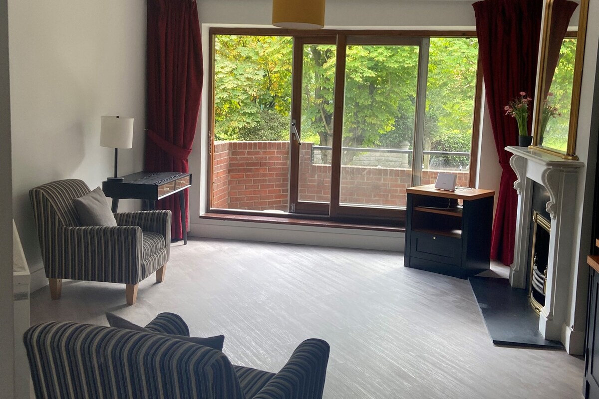 A spacious living room with a large sliding glass door leading to a balcony, a fireplace, and a striped armchair.
