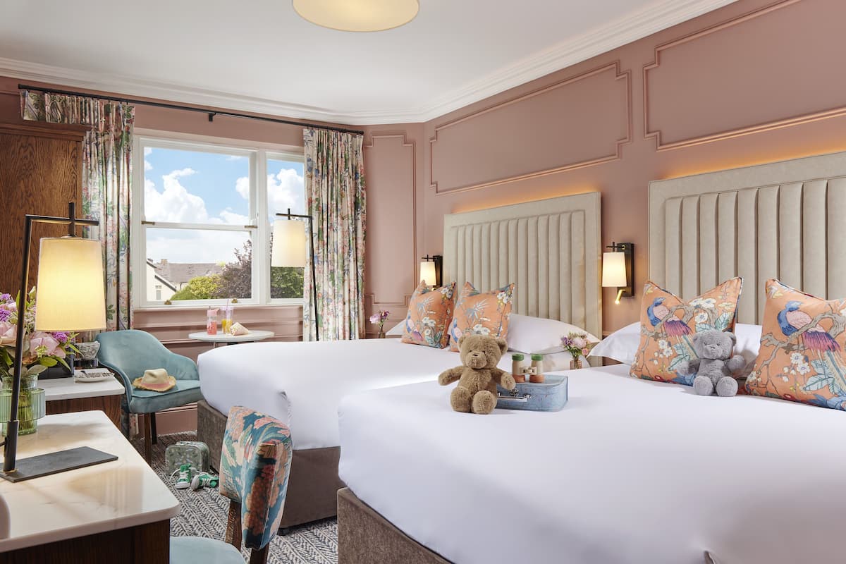 A hotel room with two beds, a sitting area with a chair, a desk, and a window with curtains.