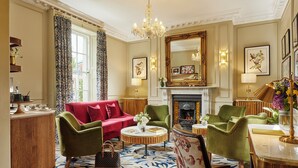 A well-appointed living room with a red sofa, green armchairs, a round coffee table, and a fireplace. - Waterloo Townhouse & Suites (Dublin)