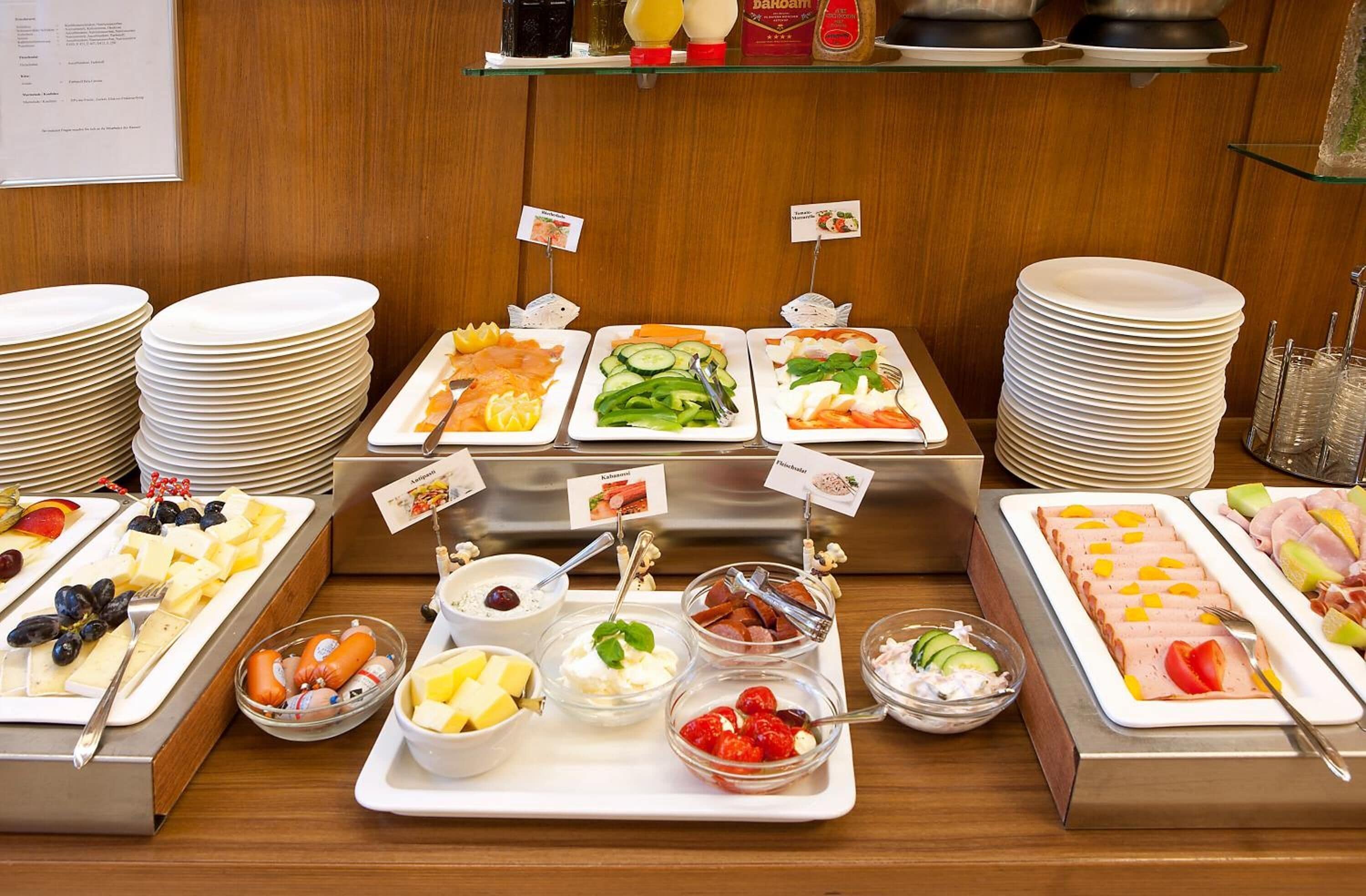A buffet with various food options, including fruits, cheeses, and meats, arranged on trays with labels.