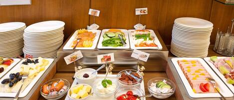 A buffet with various food options, including fruits, cheeses, and meats, arranged on trays with labels.