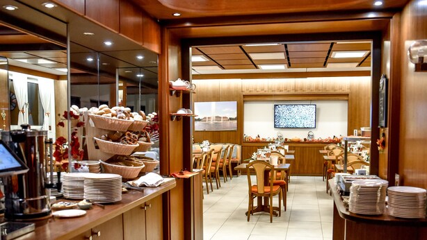 A buffet-style restaurant with multiple serving stations, chairs, and a tiled floor. - Hotel Blauer Karpfen (Oberschleissheim)