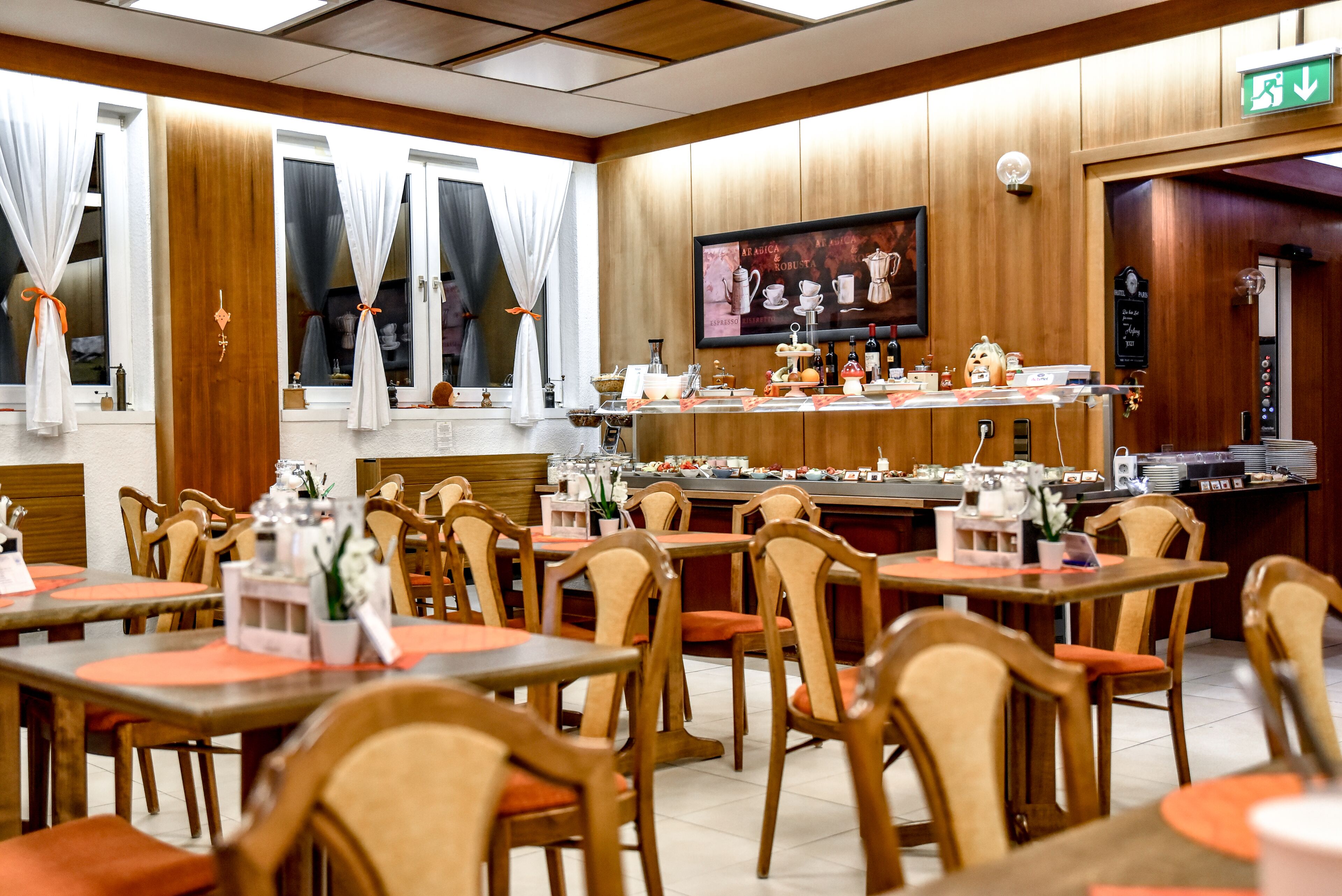A restaurant with wooden panel walls, multiple tables with orange placemats, and a bar area with various items.